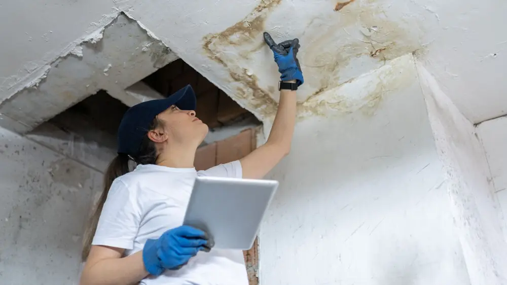Technician with a tablet inspecting a stained ceiling opening