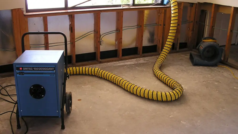 Dehumidifier with a yellow duct hose beside an opened wall